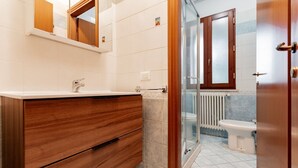 Et badeværelse med en trækommode, glasbrusekabine og et hvidt toilet.