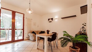 En rummelig opholdsstue med spisebord, stole, sofa og et stort vindue med gardiner.