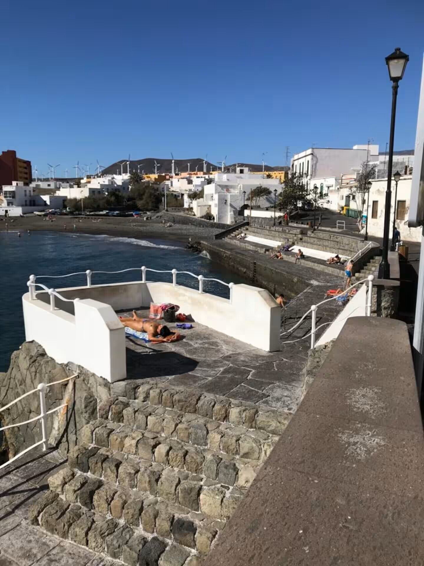 Une promenade en bord de mer, avec des escaliers en pierre menant à une plage, des bâtiments blancs et un ciel bleu azur.