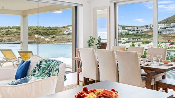 Une chambre moderne avec un coin repas, de grandes fenêtres et une vue sur la mer.