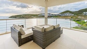 Un balcon abrité, doté de mobilier en osier et offrant une vue sur la mer et les collines.
