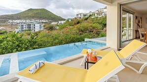 Un balcon avec une piscine, des fauteuils de jardin jaunes et une table avec des boissons.