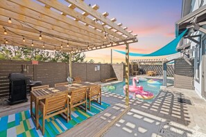 En baghave med et træpergola, grill, pool med flydende ringe og en overdækket terrasse.