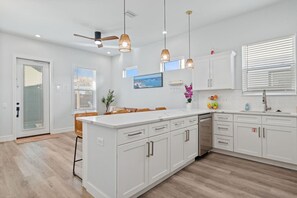 A modern kitchen with white cabinetry, a central island, pendant lighting, and a view of the ocean through the window. - *New~Heated Pool+Great Patio+Grill+Pool Table (Panama City Beach)