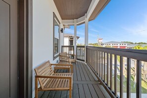A wooden deck with three wooden chairs, a railing, and a view of a building in the background. - Vincente Seascape (A) (Panama City Beach)