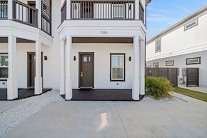 A modern two-story residential building with a balcony, a front door, and a small garden area. - Vincente Seascape (A) (Panama City Beach)