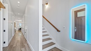 A modern hallway with a wooden staircase and a wall-mounted light fixture. - Vincente Seascape (A) (Panama City Beach)