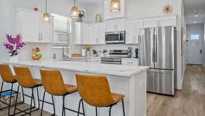 A modern kitchen with white cabinets, stainless steel appliances, and a central island with bar stools. - Vincente Seascape (A) (Panama City Beach)