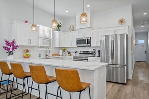 A modern kitchen with white cabinets, stainless steel appliances, and a central island with bar stools. - Vincente Seascape (A) (Panama City Beach)