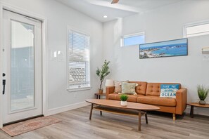 Uma sala de estar moderna com uma mesa de centro de madeira, um sofá marrom e uma pintura com paisagem costeira.