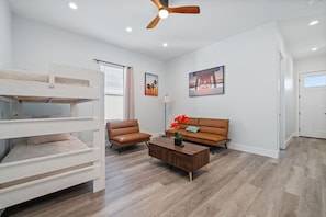 A modern living room with a bunk bed, a brown leather sofa, a wooden coffee table, and a ceiling fan. - Vincente Seascape (A) (Panama City Beach)
