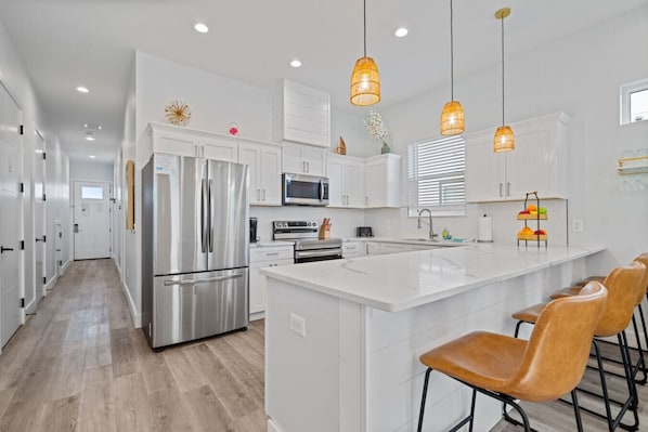 A modern kitchen with white cabinetry, stainless steel appliances, a large island with bar stools, and pendant lighting.