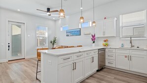 Een moderne keuken met witte kastjes, een centraal eiland, hanglampen en uitzicht op de oceaan door het raam.