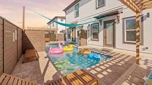 Een achtertuin met een zwembad, een houten terras en een pergola.