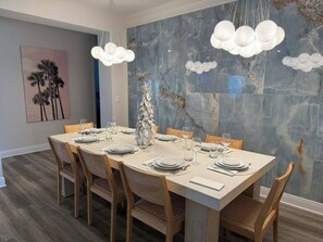 Un comedor con una pared de mármol, una mesa grande preparada para seis personas y un centro de mesa original.