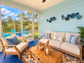 A sunroom with a sofa, chairs, and a coffee table. There are windows, a view of the outdoors, and decorative wall art.