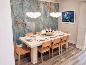 Ein Esszimmer mit Marmorwand, einem modernen Kronleuchter und einem gerahmten abstrakten Gemälde.