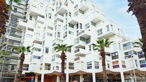 Un edificio de varios pisos con balcones, palmeras y cielo despejado.