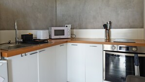 Una cocina con gabinetes blancos, microondas, estufa y pileta.
