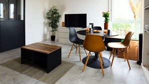 Una sala de estar moderna con comedor, que incluye un televisor de pantalla plana, una mesa de centro de madera y una planta en maceta.