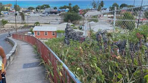 A coastal road with a metal guardrail, a pedestrian, and a view of the ocean and buildings in the distance.