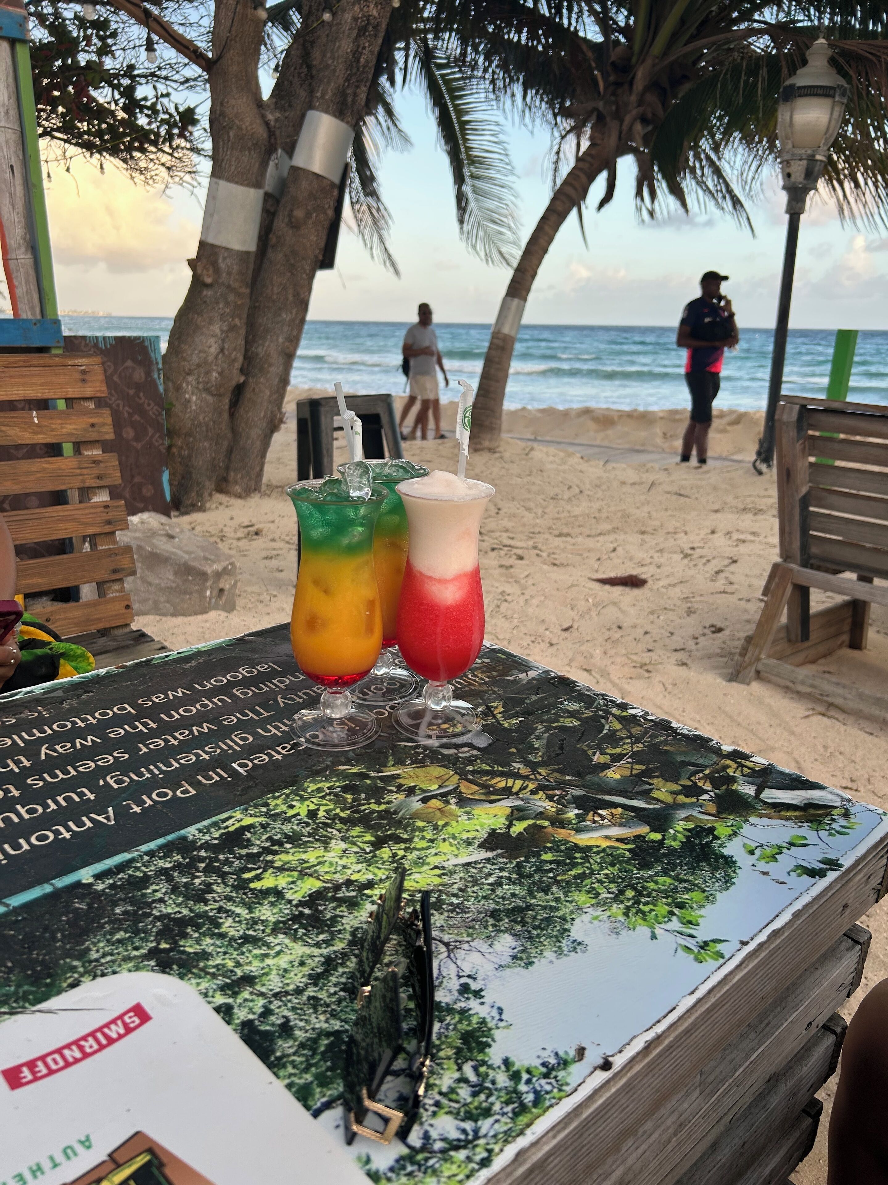 A beachside table with colorful drinks and a menu.