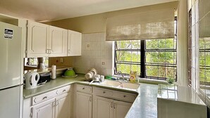 A compact kitchen with white cabinets, a built-in refrigerator, and a window with a view of greenery.
