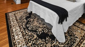 A bedroom with a large bed, a chandelier, wooden beams, and a patterned rug.