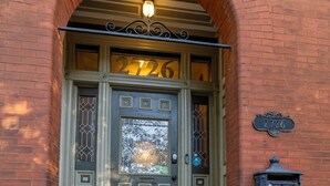 A brick building entrance with a green door, a number plaque, and a mailbox.