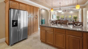 A kitchen with wooden cabinets, a stainless steel refrigerator, granite countertops, and pendant lighting. - NEW 3 BDR villa near Jolly Hall beach and Turtle beach in Welcoming George Town (George Town)