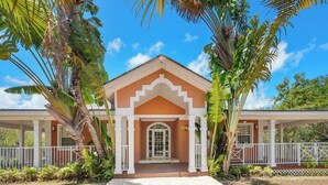 A two-story building with a central entrance, surrounded by palm trees and a white fence. - NEW 3 BDR villa near Jolly Hall beach and Turtle beach in Welcoming George Town (George Town)