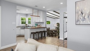 Une cuisine moderne avec des meubles blancs, un îlot central en bois et un coin repas comprenant une table et des chaises.