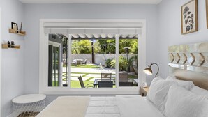 A bedroom with a large bed, a bedside lamp, a view of the backyard through a sliding door, and a small round table with a chair. - UPSCALE & UPGRADED 3BR HOUSE in ENCINO with GARAGE & LARGE FENCED YARD/PATIO p84 (Los Angeles)