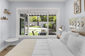 A bedroom with a large bed, a bedside lamp, a view of the backyard through a sliding door, and a small round table with a chair. - UPSCALE & UPGRADED 3BR HOUSE in ENCINO with GARAGE & LARGE FENCED YARD/PATIO p84 (Los Angeles)