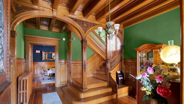 A grand staircase with ornate woodwork, a chandelier, and a floral arrangement. - Victoria Mansion 1895, Near SBU - AA Milne Room! (Olean)