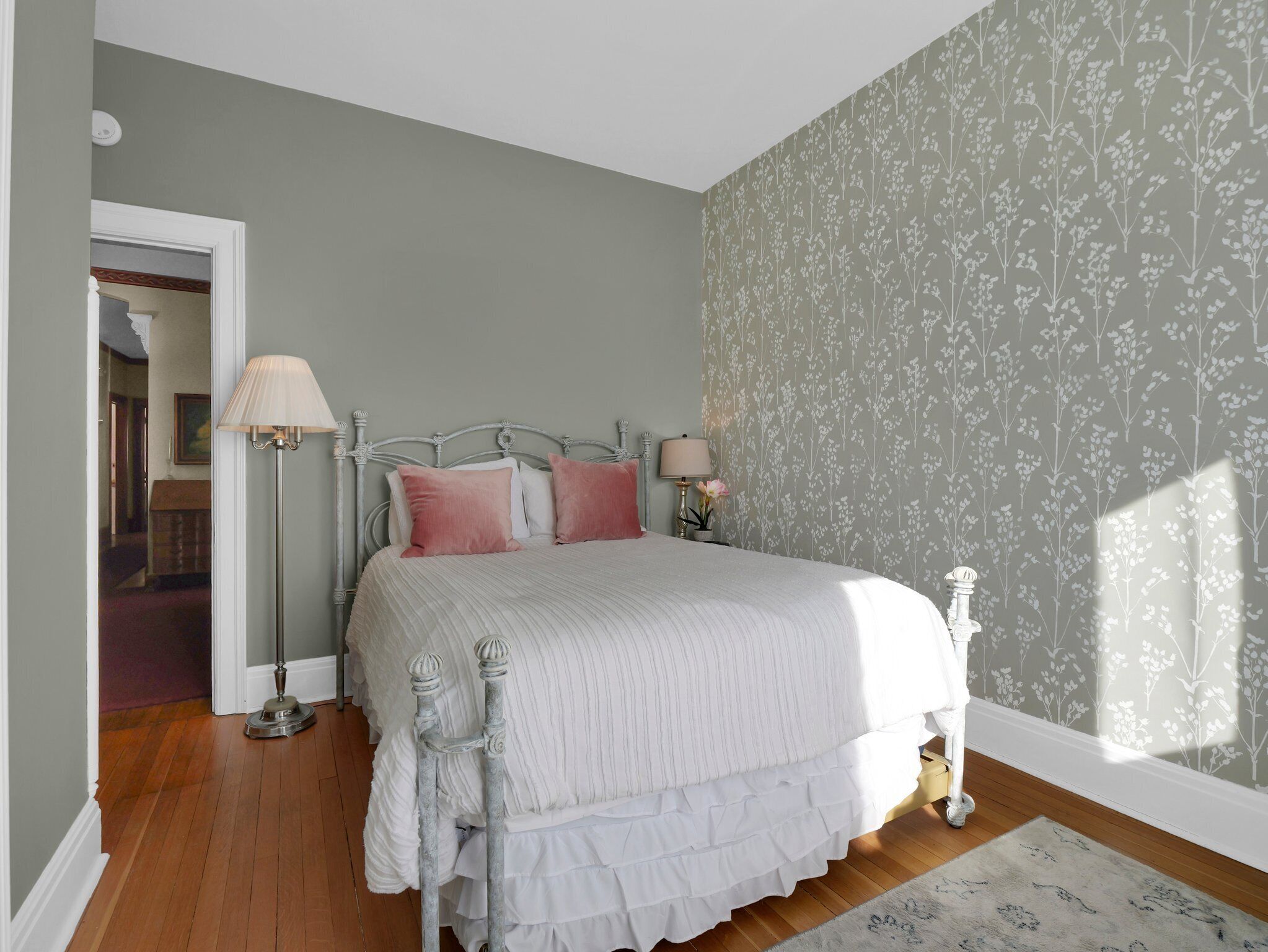 Un dormitorio con cama, dos lámparas de noche, falda de cama con vuelo y papel tapiz floral.