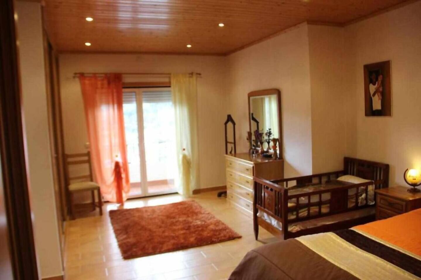 A bedroom with a wooden ceiling, a dresser, a bed, a desk, and a chair.