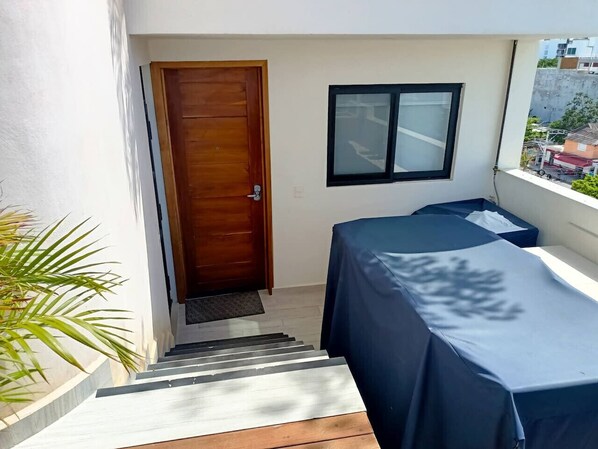 A small balcony with a wooden door, a window, and a covered table.
