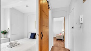 Ett modernt hotellrum med en snyggt bäddad säng, en garderob i trä och en hall som leder till en matplats.