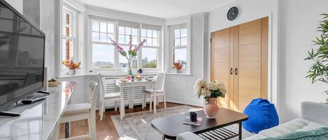 A modern living room with a TV, a dining area with a table and chairs, and a large window with a view.
