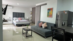 A modern, well-lit living room with a large bed, a sofa, a dining table, and a refrigerator. - Nirvana ApartaHotel (Cali)