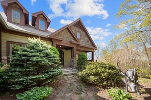 A two-story house with a stone pathway leading to the front door, surrounded by various shrubs and a deer sculpture.