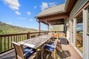 A wooden deck with a table and chairs, a covered area, and a view of the surrounding landscape.
