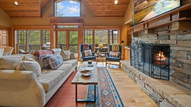 A spacious living room with a stone fireplace, large windows, and a cozy seating area. - Mountain Home with Mountain Views (Sugar Mountain)