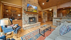 A cozy living room with a stone fireplace, wooden shelves, and a large TV mounted above it. - Mountain Home with Mountain Views (Sugar Mountain)