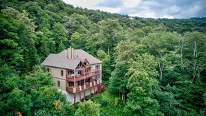 A two-story house surrounded by dense forest, with a balcony overlooking the greenery. - Mountain Home with Mountain Views (Sugar Mountain)