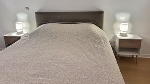 A neatly made bed with a patterned bedspread, flanked by two bedside tables with lamps, in a simple room with a plain wall and a wooden floor. - Entre Port & Mer - Spacious 77m2 apartment in Dieppe (Dieppe)