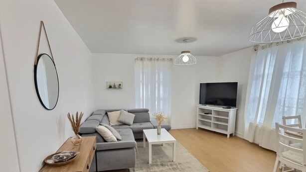 A modern living room with a grey sofa, a white coffee table, a TV on a white stand, and a hanging light fixture. - Entre Port & Mer - Spacious 77m2 apartment in Dieppe (Dieppe)