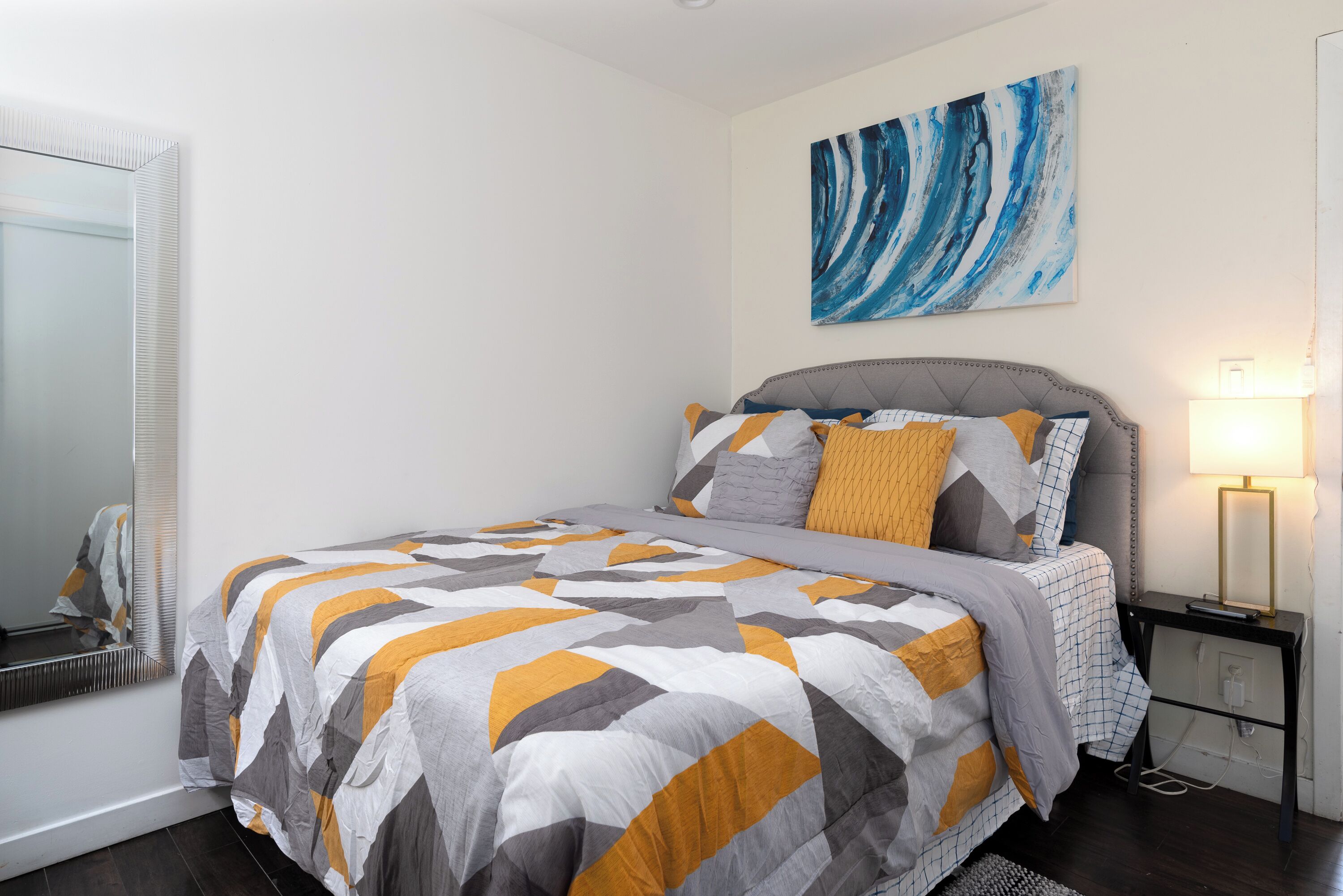 Une chambre à coucher avec un lit, une table de chevet, une lampe et un tableau au mur.