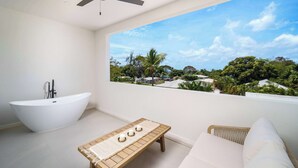 Un bagno moderno con una vasca freestanding, una ventola a soffitto e vista su un paesaggio rigoglioso attraverso un'ampia finestra.